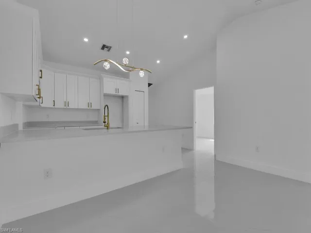 Kitchen with white cabinetry, pendant lighting, sink, lofted ceiling, and light tile patterned floors