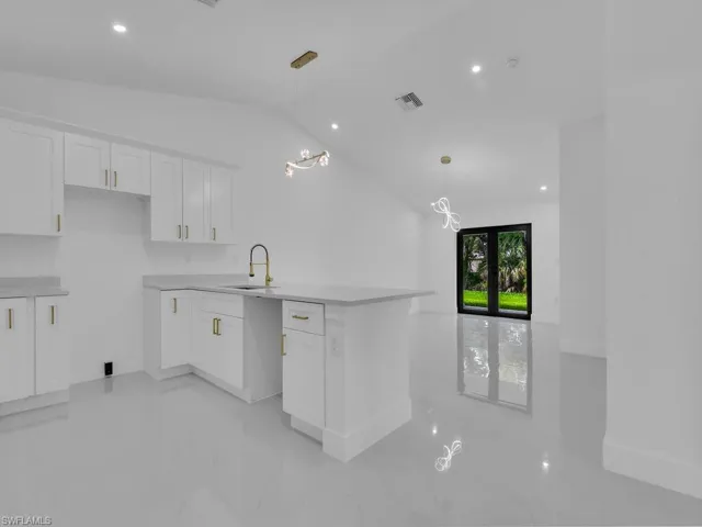 Kitchen featuring hanging light fixtures, sink, white cabinetry, and vaulted ceiling
