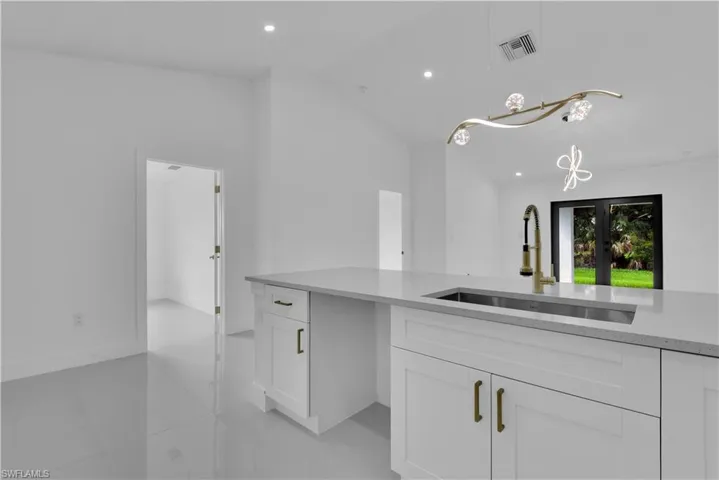 Kitchen with vaulted ceiling, sink, decorative light fixtures, light tile patterned flooring, and white cabinetry