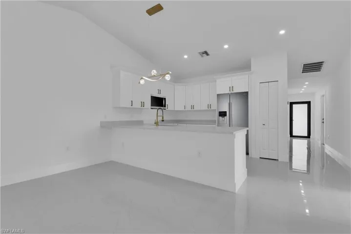 Kitchen with light tile patterned flooring, appliances with stainless steel finishes, white cabinets, and vaulted ceiling