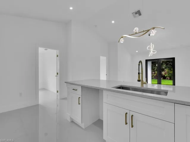 Kitchen featuring light tile patterned flooring, lofted ceiling, white cabinetry, hanging light fixtures, and sink