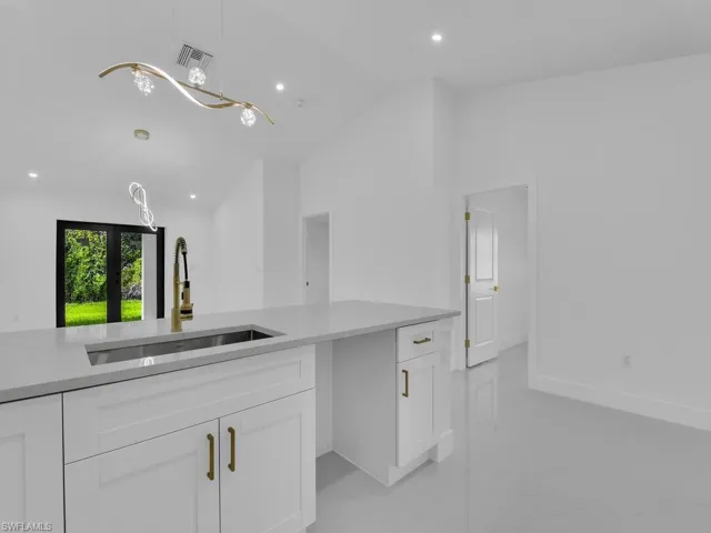 Kitchen featuring vaulted ceiling, sink, hanging light fixtures, light tile patterned floors, and white cabinetry