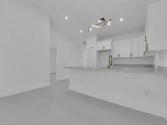 Kitchen with white cabinetry, pendant lighting, sink, lofted ceiling, and light tile patterned floors