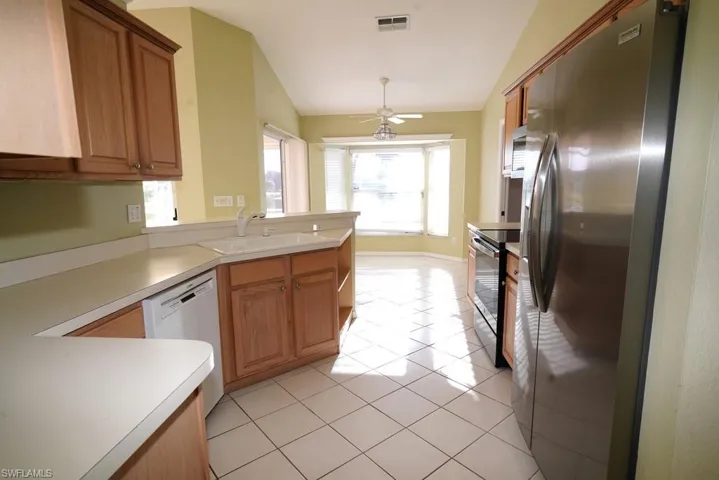 Kitchen featuring appliances with stainless steel finishes, light tile patterned floors, lofted ceiling, light countertops, and brown cabinets