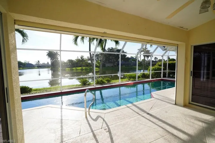 Outdoor pool with a sunroom, a water view, glass enclosure, and a patio area