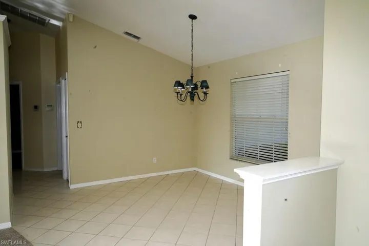 Unfurnished dining area with a chandelier, light tile patterned flooring, and vaulted ceiling