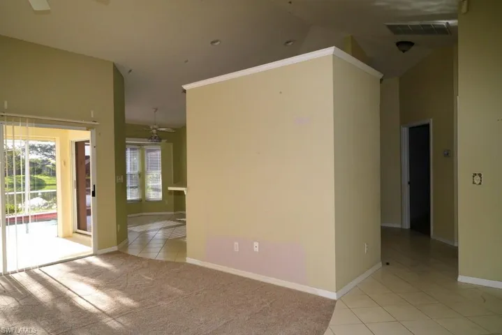 Empty room with light tile patterned flooring, ceiling fan, light colored carpet, and vaulted ceiling
