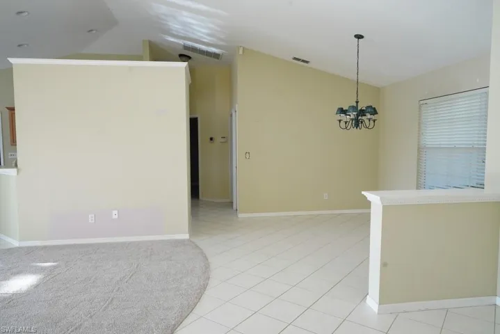 Empty room with vaulted ceiling, light tile patterned flooring, and a chandelier