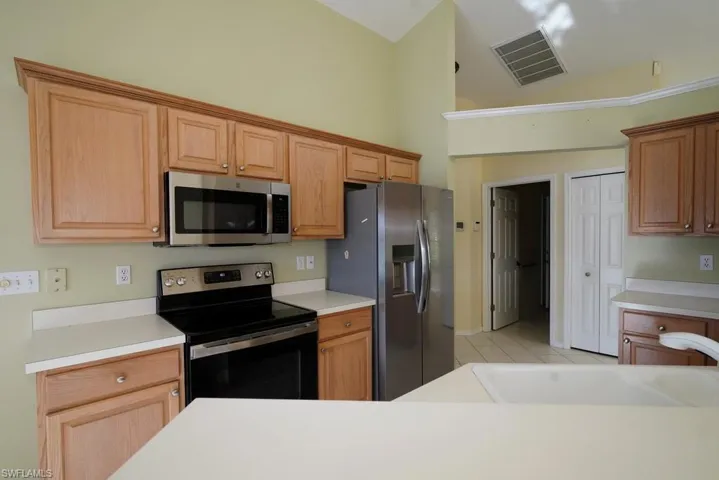 Kitchen with stainless steel appliances, light countertops, high vaulted ceiling, and light brown cabinetry