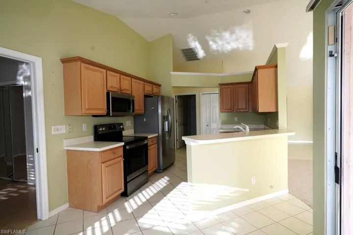 Kitchen featuring appliances with stainless steel finishes, a peninsula, light tile patterned flooring, light countertops, and high vaulted ceiling