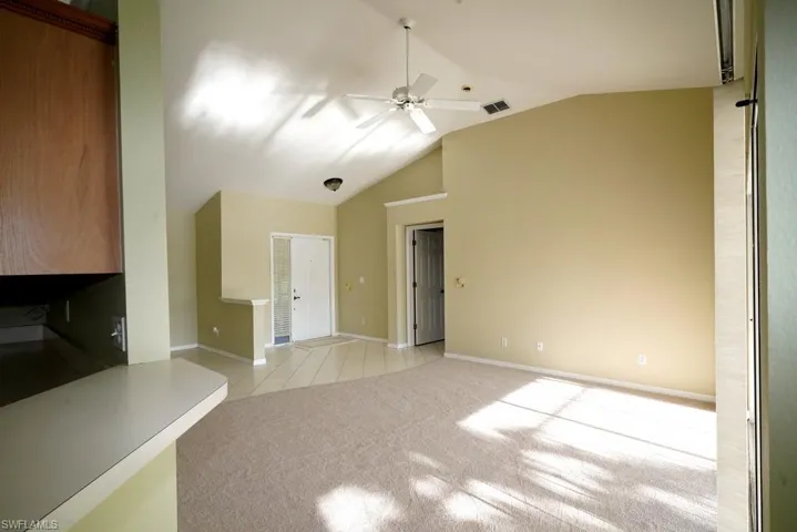 Unfurnished living room with light carpet, ceiling fan, light tile patterned flooring, and high vaulted ceiling