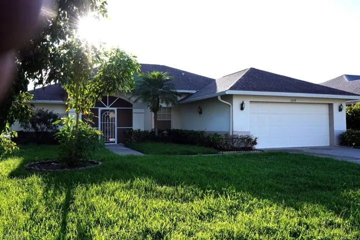 Single story home with stucco siding, roof with shingles, driveway, and a front lawn