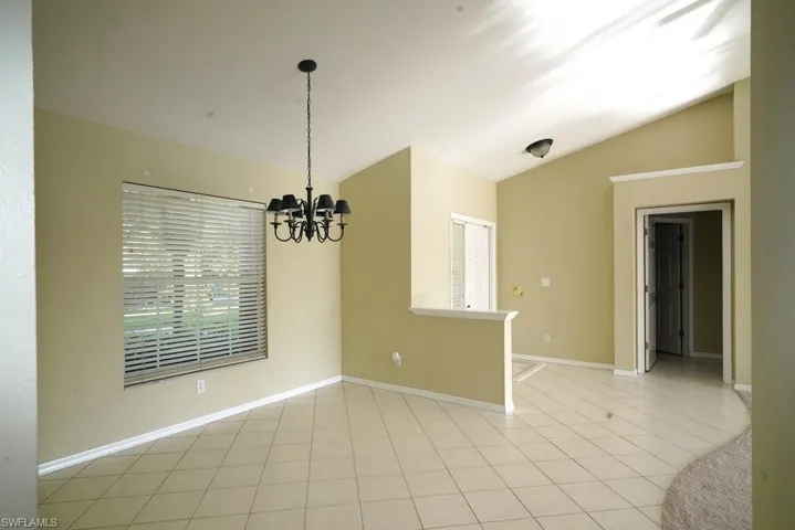 Empty room with lofted ceiling, a chandelier, and light tile patterned floors