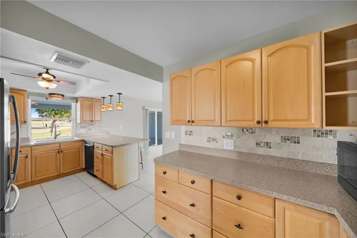 Kitchen featuring ceiling fan, sink, kitchen peninsula, decorative light fixtures, and light brown cabinetry