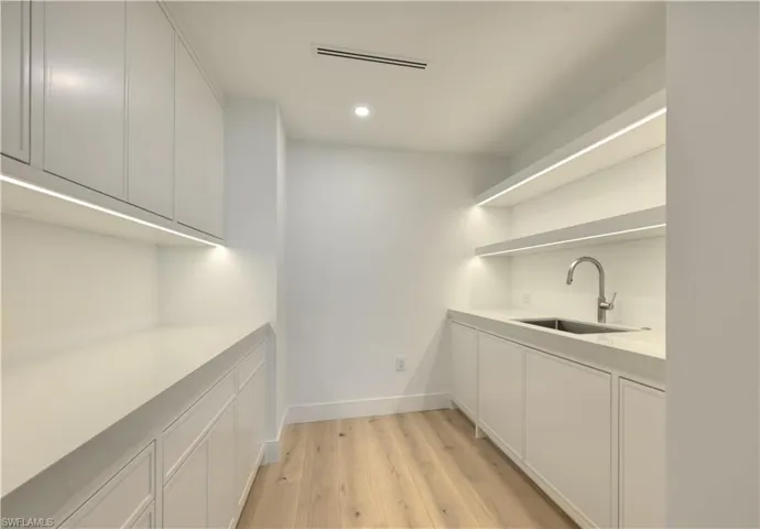 Bar featuring sink, light wood-type flooring, and white cabinets