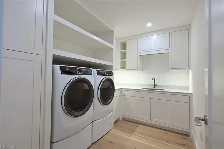 Laundry area featuring cabinets, washing machine and clothes dryer, light hardwood / wood-style flooring, and sink