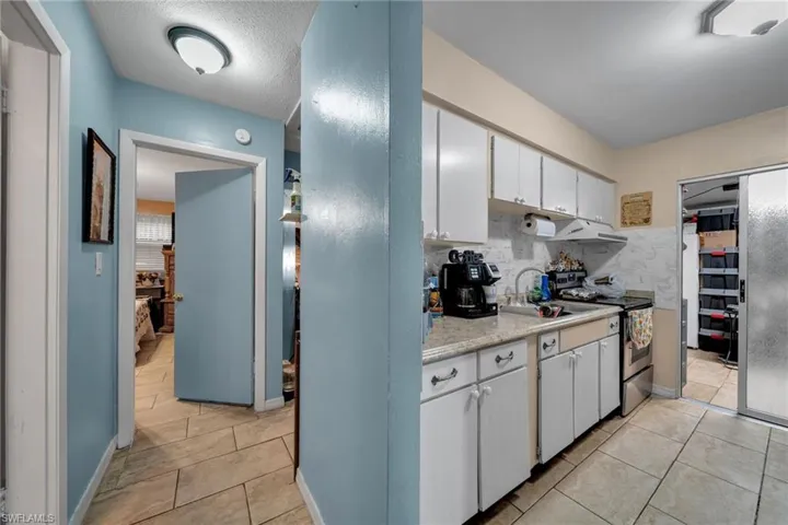 Kitchen featuring stainless steel range with electric stovetop, light countertops, light tile patterned flooring, white cabinets, and backsplash