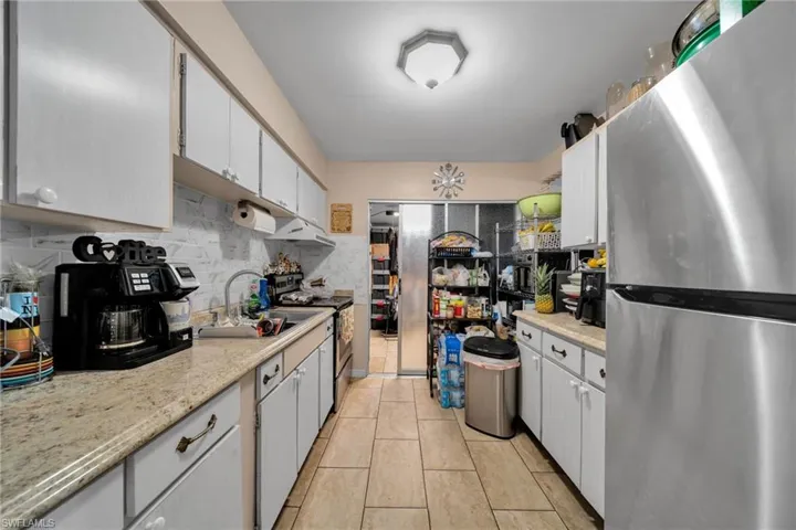 Kitchen with stainless steel appliances, backsplash, light tile patterned floors, and white cabinetry