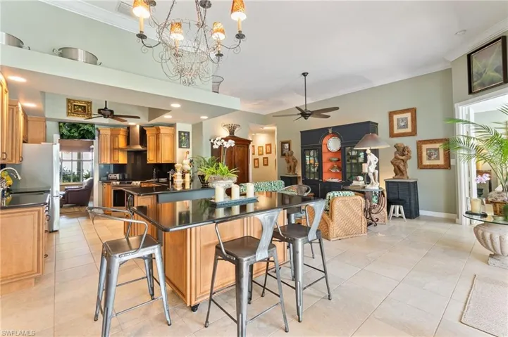 Kitchen with a ceiling fan, a kitchen breakfast bar, ornamental molding, wall chimney exhaust hood, and pendant lighting
