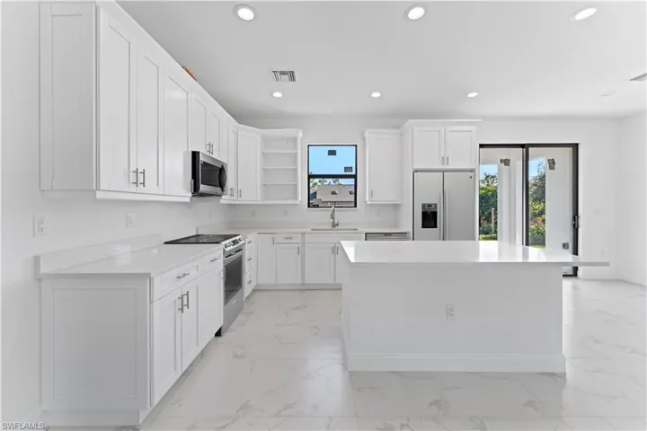 Kitchen featuring white cabinets, appliances with stainless steel finishes, a kitchen island, and sink