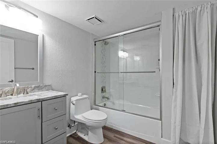 Full bathroom featuring vanity, toilet, combined bath / shower with glass door, and hardwood / wood-style flooring