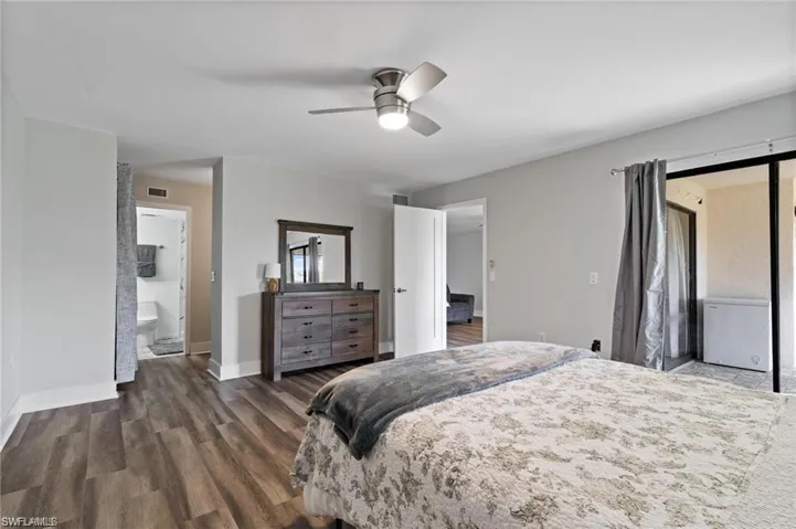 Bedroom featuring dark wood-type flooring, ceiling fan, a barn door, and ensuite bath