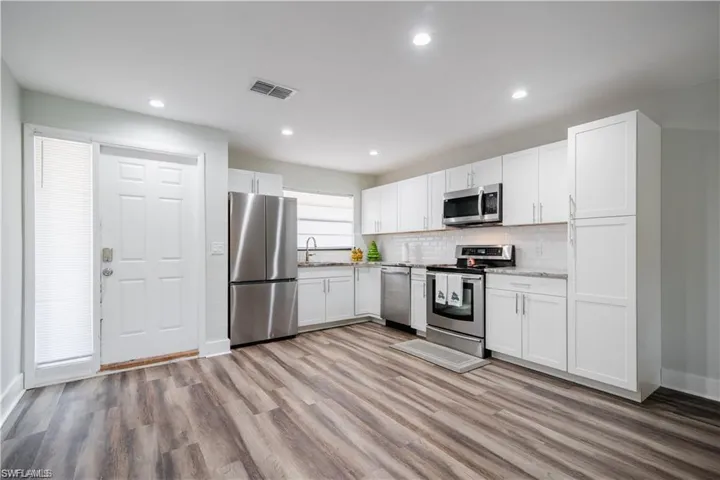 Kitchen featuring stainless steel appliances, hardwood / wood-style floors, decorative backsplash, and white cabinetry