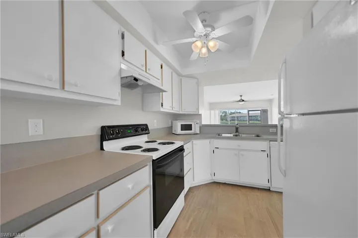 Kitchen with light hardwood / wood-style flooring, white appliances, sink, white cabinetry, and ceiling fan