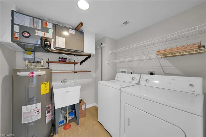Washroom with electric water heater, sink, light hardwood / wood-style flooring, and washer and dryer