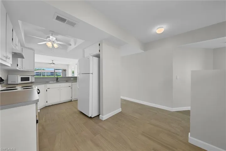Kitchen featuring white appliances, light wood-type flooring, white cabinets, ventilation hood, and ceiling fan