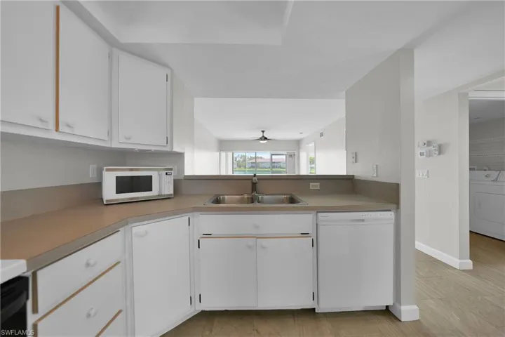 Kitchen featuring white cabinetry, ceiling fan, white appliances, sink, and washer / clothes dryer