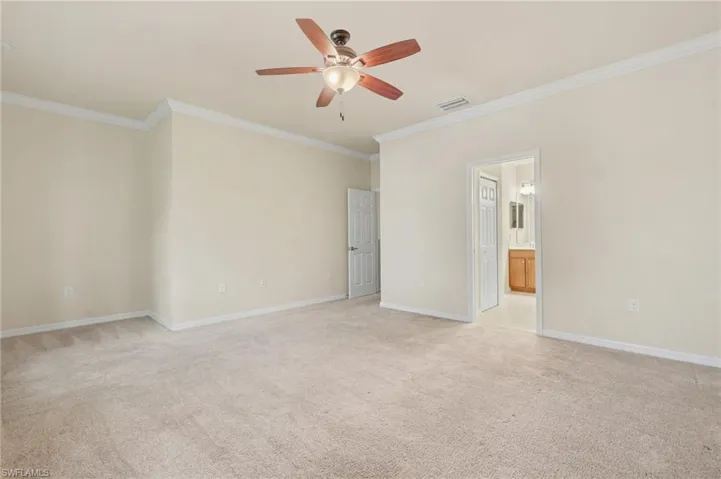 Spare room featuring light colored carpet, crown molding, and a ceiling fan
