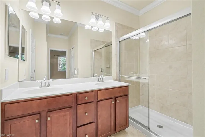 Full bathroom featuring crown molding, double vanity, and a shower stall