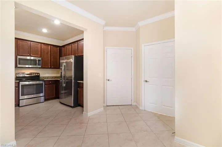 Kitchen featuring appliances with stainless steel finishes, dark brown cabinetry, ornamental molding, light tile patterned flooring, and light stone counters
