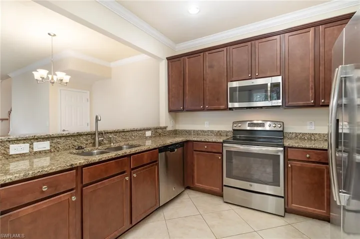 Kitchen with stainless steel appliances, light stone counters, ornamental molding, and pendant lighting