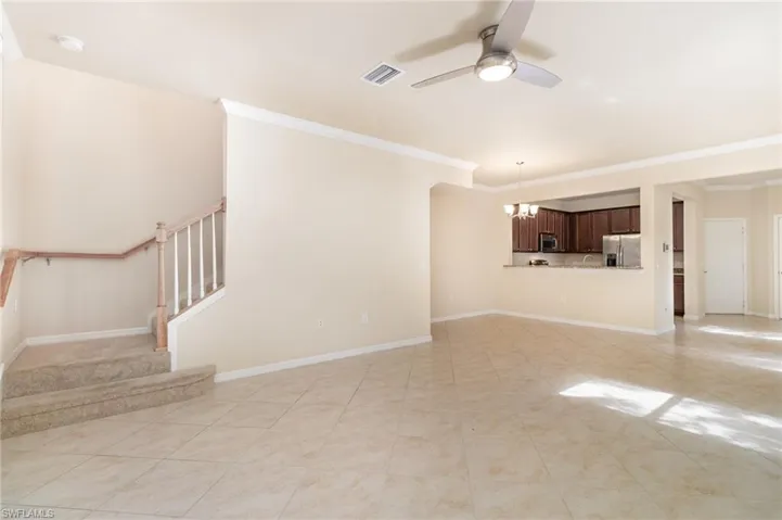 Unfurnished living room featuring ceiling fan, ornamental molding, a chandelier, stairs, and light tile patterned floors