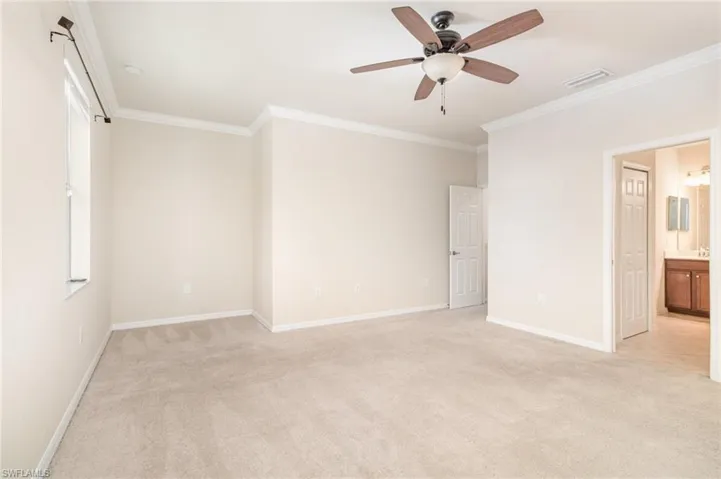 Unfurnished bedroom featuring light carpet, crown molding, ceiling fan, and ensuite bath