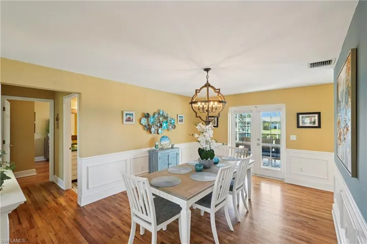 Dining room featuring suspended lighting, wood finished floors, wainscoting, and french doors