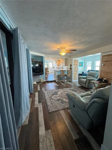 Living area featuring a textured ceiling, dark wood-style flooring, and a ceiling fan