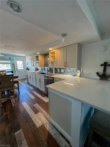 Kitchen with dishwasher, a peninsula, glass insert cabinets, backsplash, and dark wood-style floors