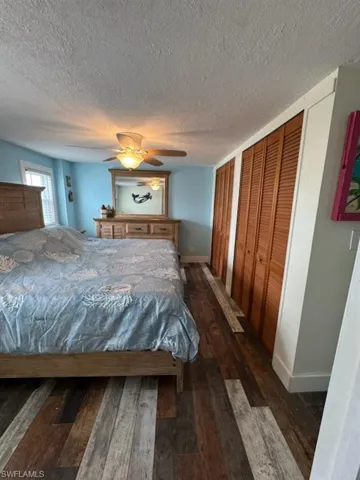 Bedroom featuring dark wood-style flooring, two closets, a textured ceiling, and a ceiling fan