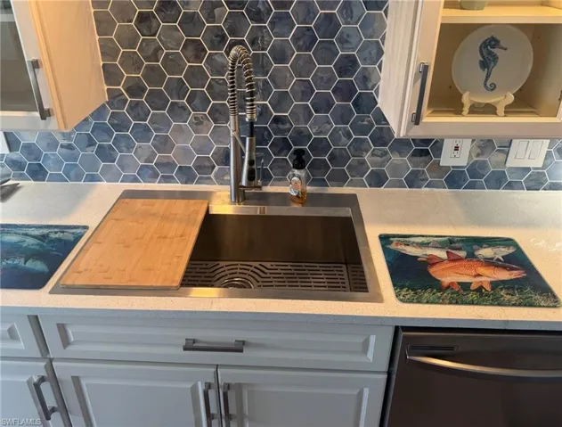 Kitchen view of tasteful backsplash, dishwasher, light countertops, and white cabinets