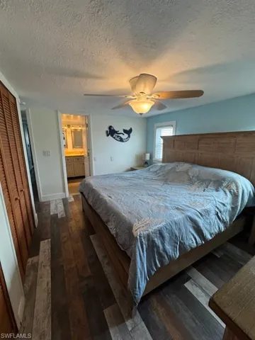 Bedroom with wood-type flooring, a textured ceiling, a ceiling fan, 2 closets, and connected bathroom