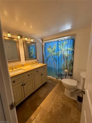 Bathroom featuring stone tile floors, double vanity, and curtained shower