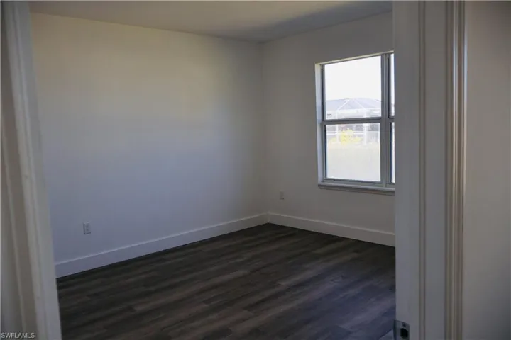 Spare room with dark wood-style floors and baseboards