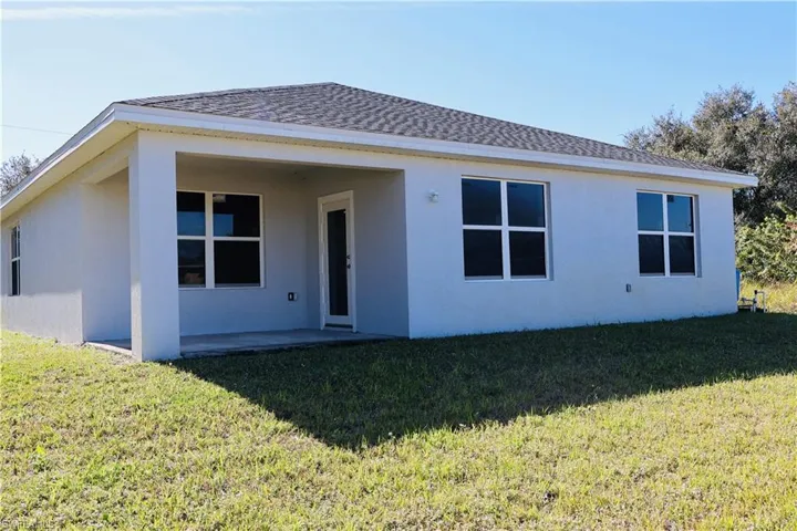 Back of property with a patio area, stucco siding, a lawn, and roof with shingles