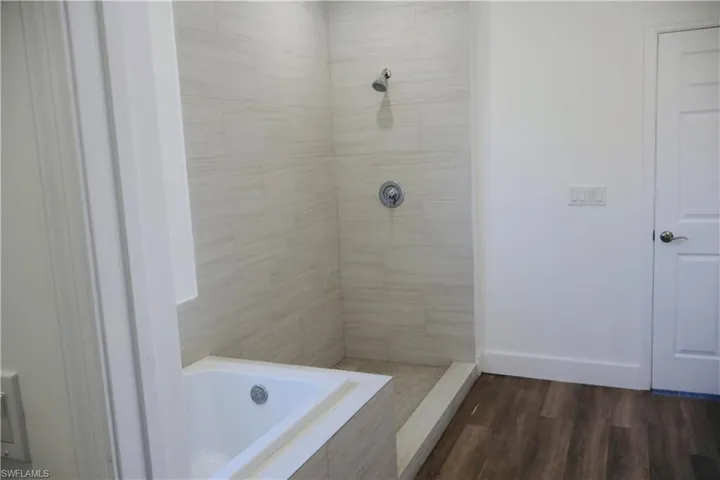 Full bathroom featuring a garden tub, dark wood-type flooring, and a tile shower