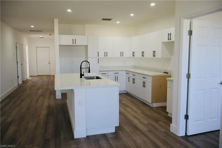 Kitchen with white cabinetry, light stone countertops, a kitchen island with sink, dark wood finished floors, and recessed lighting