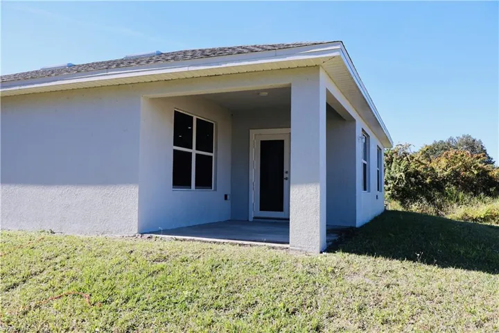 View of exterior entry featuring stucco siding, a patio area, and a yard