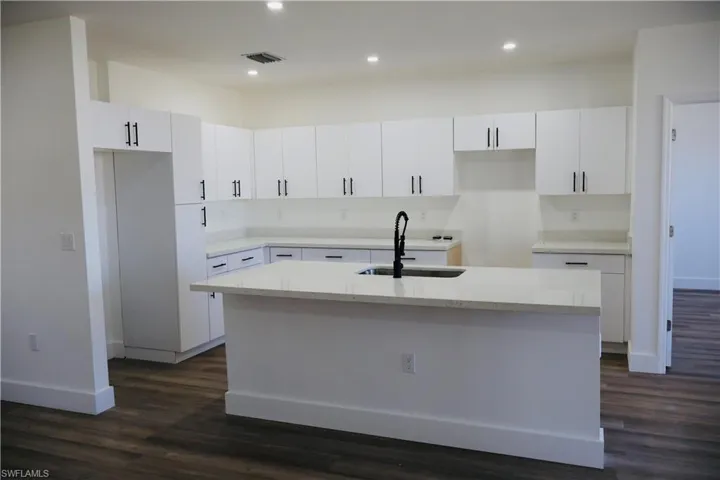 Kitchen featuring white cabinetry, dark wood-style floors, a center island with sink, light stone counters, and recessed lighting